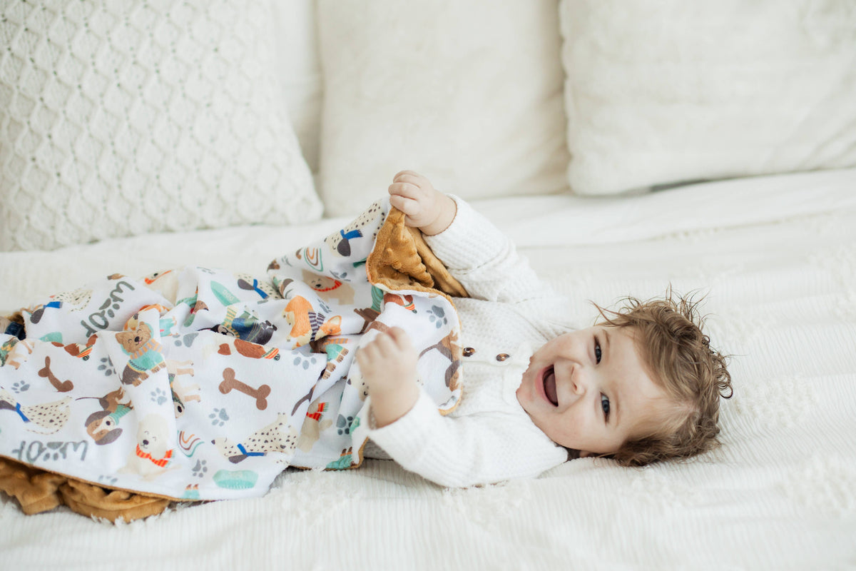 Baby lying on a couch and holding a blanket with a dog pattern