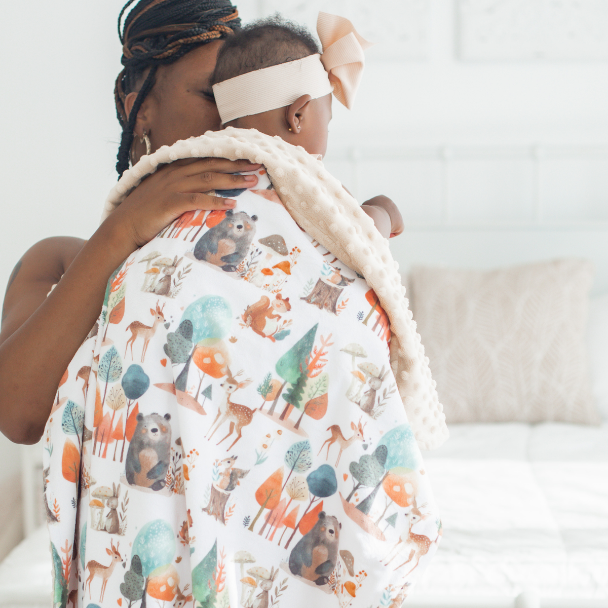 Mom holding baby wearing a bow and an enchanted forest themed blanket