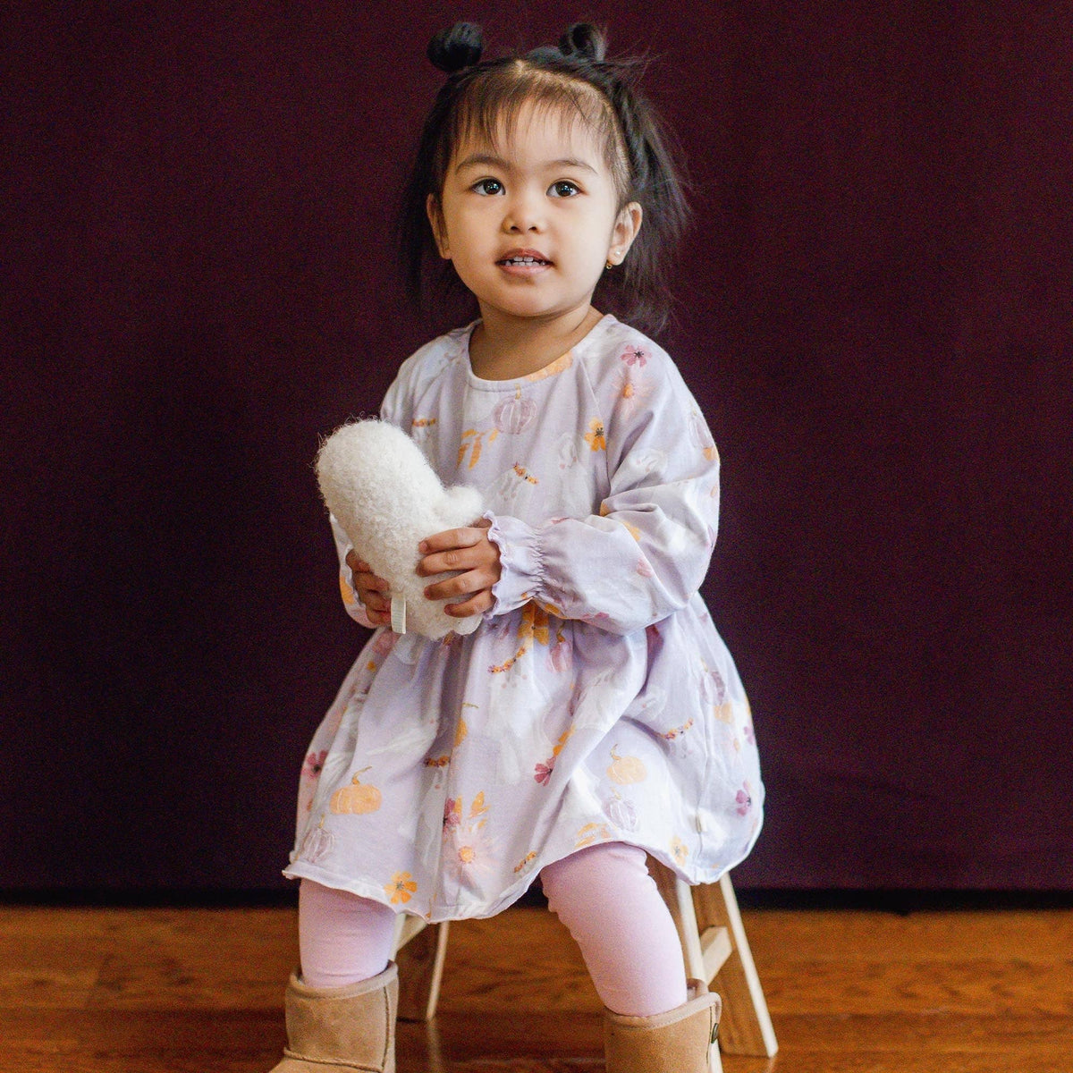 Child in a light purple dress holding a plush toy against a dark purple background