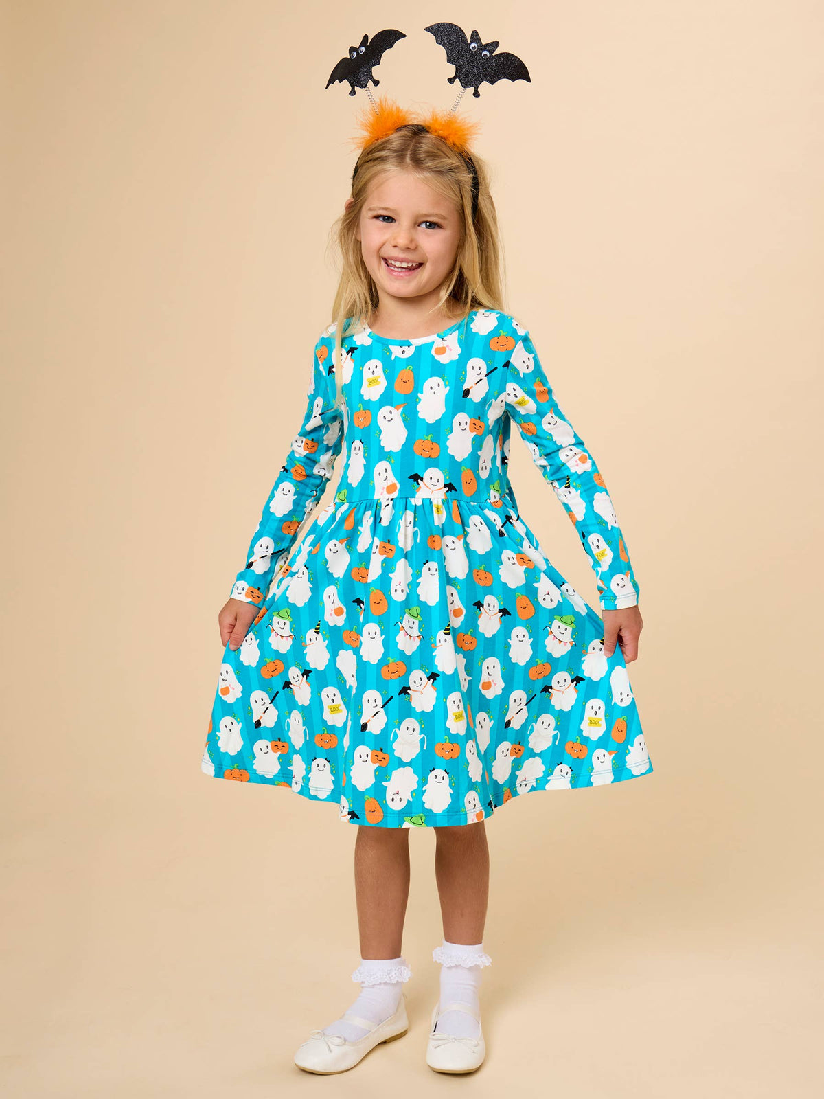 Girl in aqua long sleeve dress with ghost and pumpkin pattern against a tan background