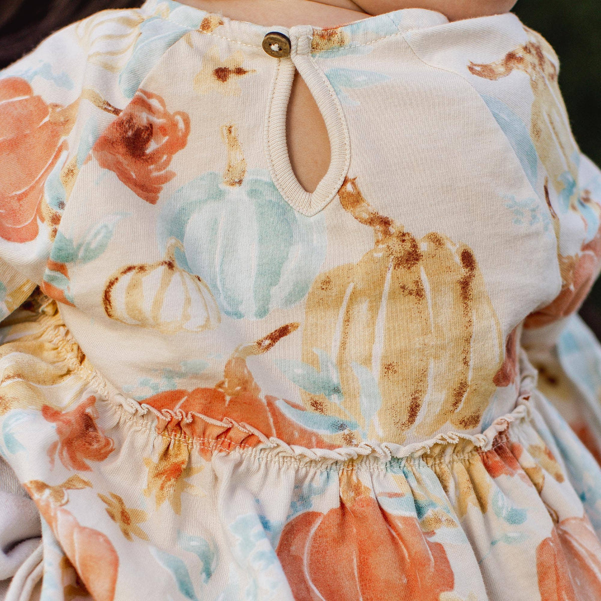 Close-up of a baby's floral dress with pumpkins and leaves.