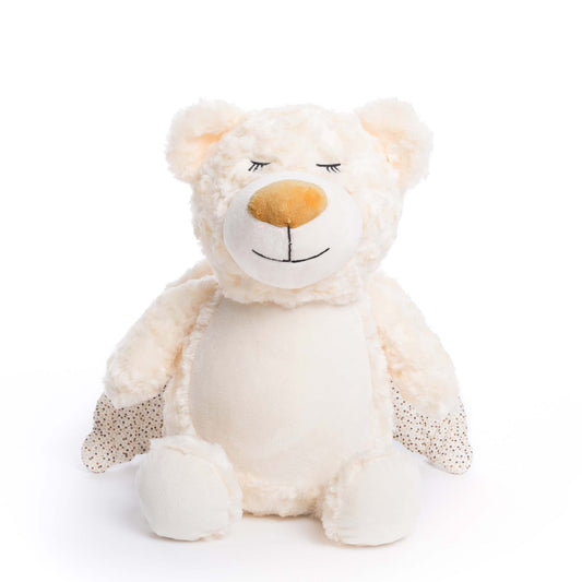 A plush cream colored bear sits serenely with its polka dot wings laid against its body against a white background. 
