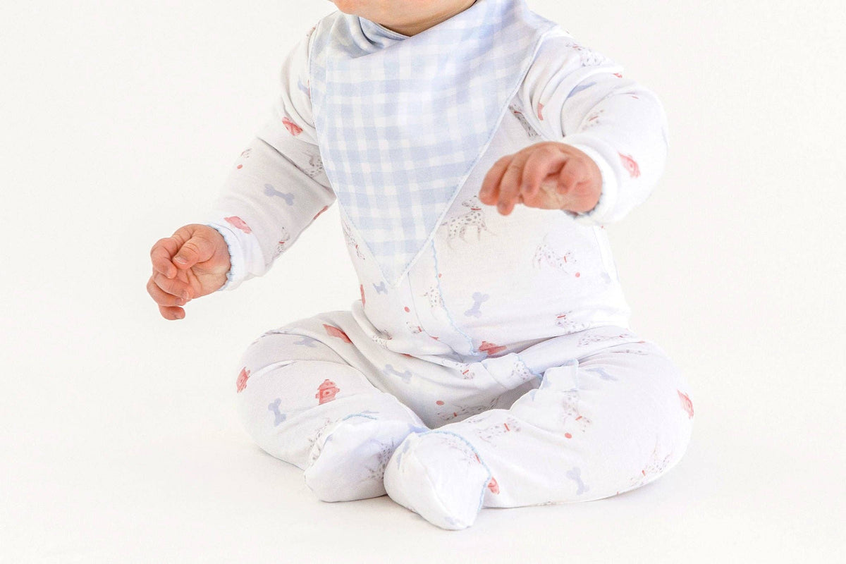 Baby wearing a onesie with a dalmation dog print and a blue checked bandana on a white background. 