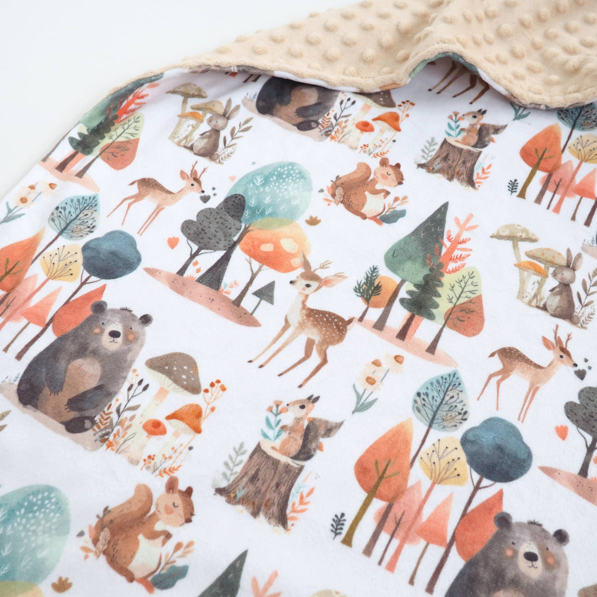 Close up of enchanted forest themed blanket on a white background with a tan reverse side
