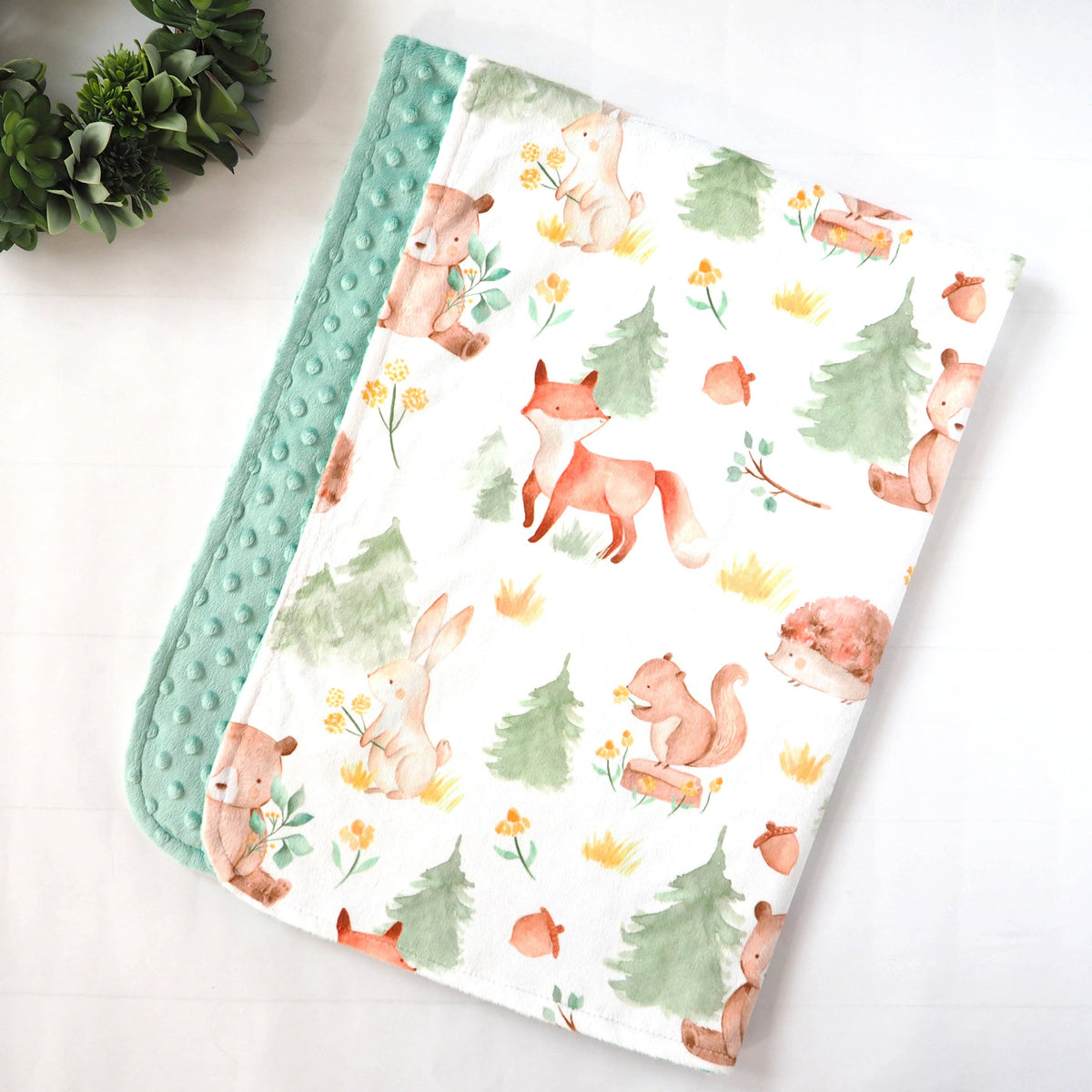 Blanket with a forest theme showing pine trees and bears, foxes, and bunnies on a white background