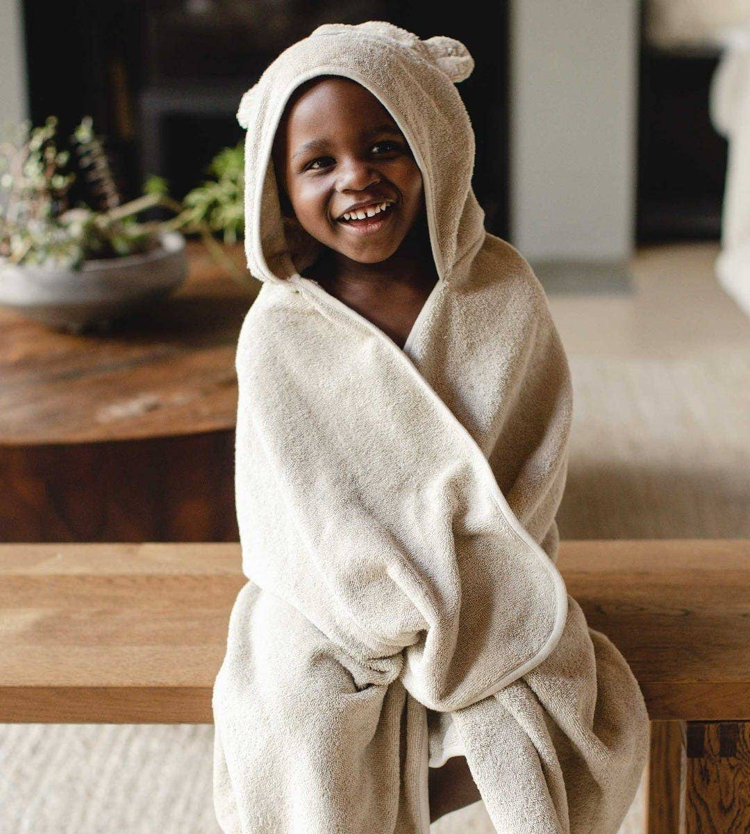Child wearing a beige towel with a hooded bear head against a room background. 