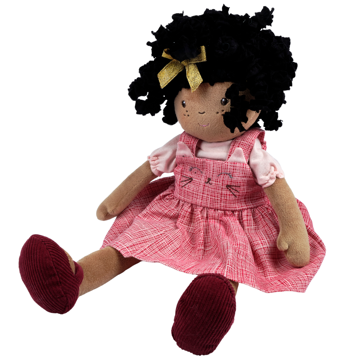 A plush doll with black curly hair, a gold bow, a pink plaid dress over a light pink shirt, and dark red shoes, shown against a plain white background.