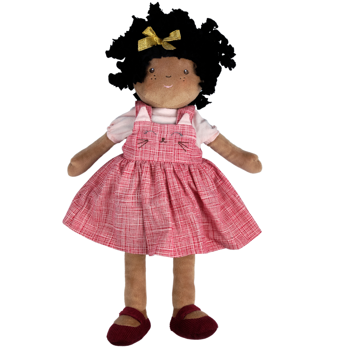 A plush doll with dark curly hair, a gold bow, and a pink plaid pinafore dress over a white shirt, standing against a plain white background.