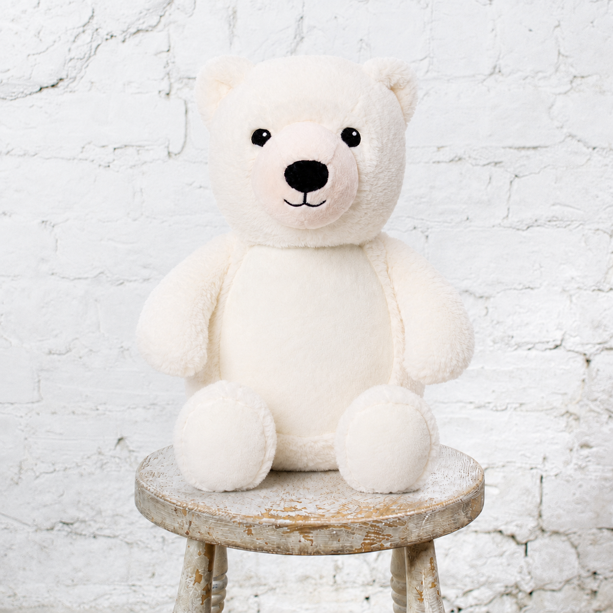White stuffed polar bear sits on a stool in front of a white wall