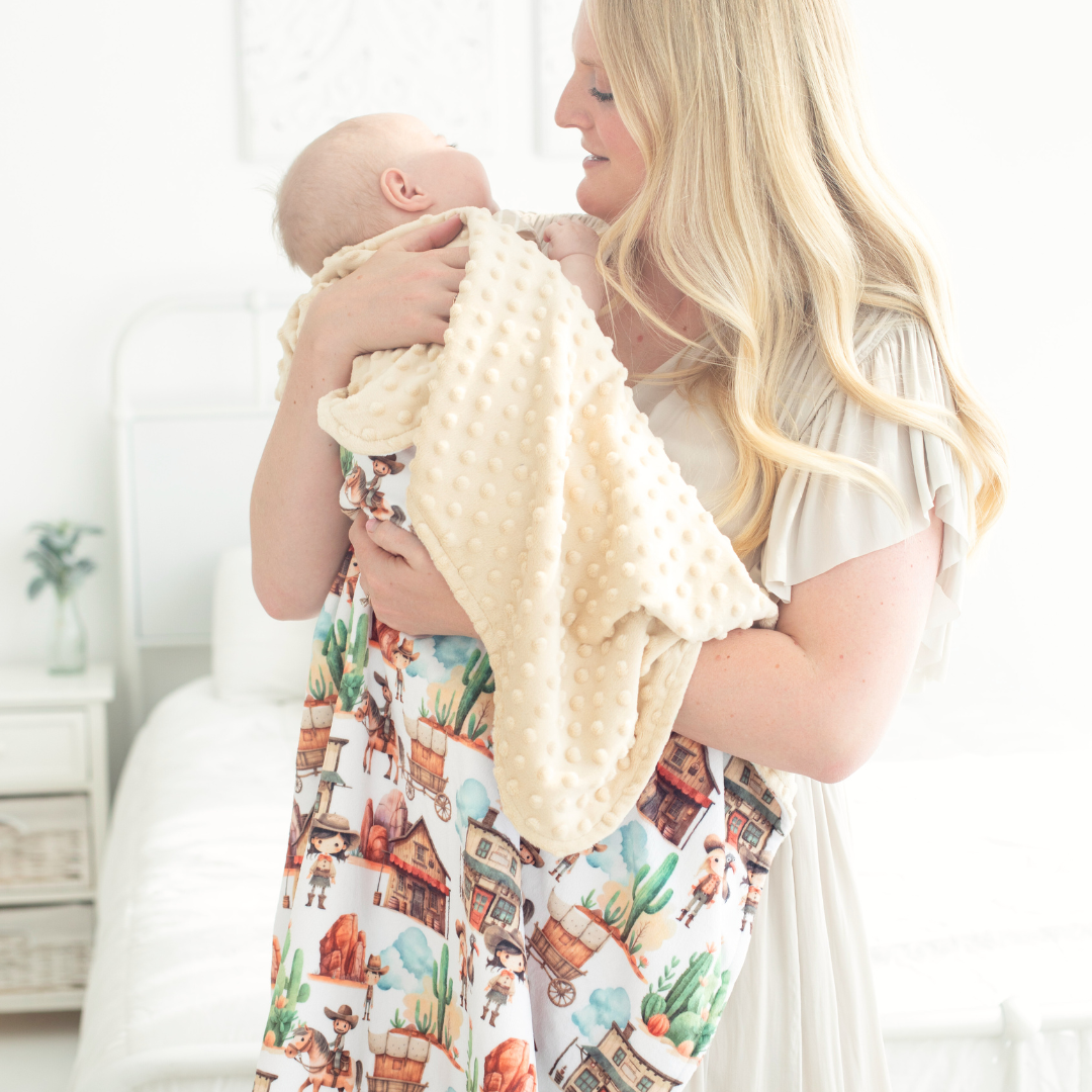 Woman holding a baby in a Western themed blanket  with a tan backside