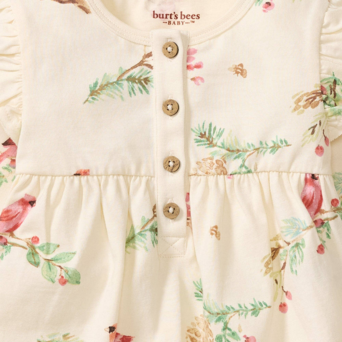 Close up of cream colored romper with buttons up the front and a cardinal pattern and a Burt's Bees Baby logo 