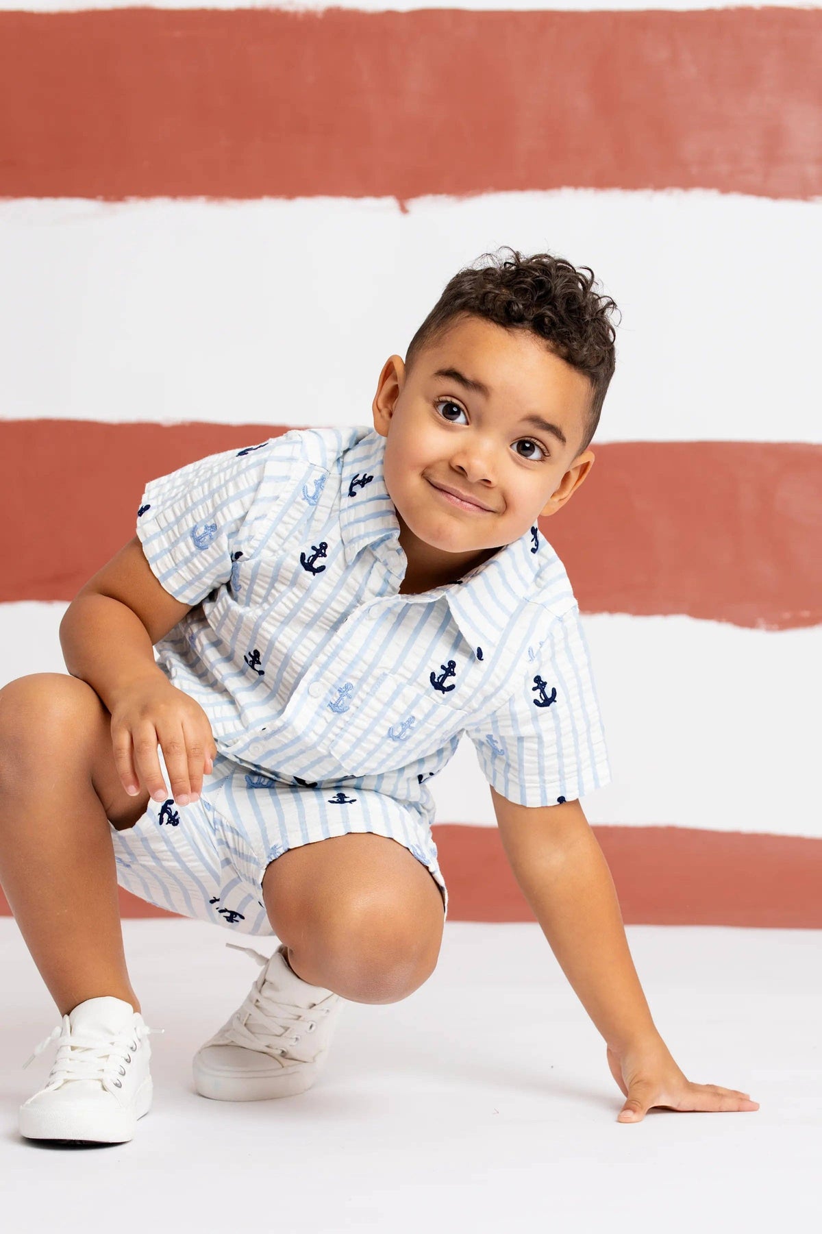 Child wearing a white outfit with blue patterns on a red and white striped background