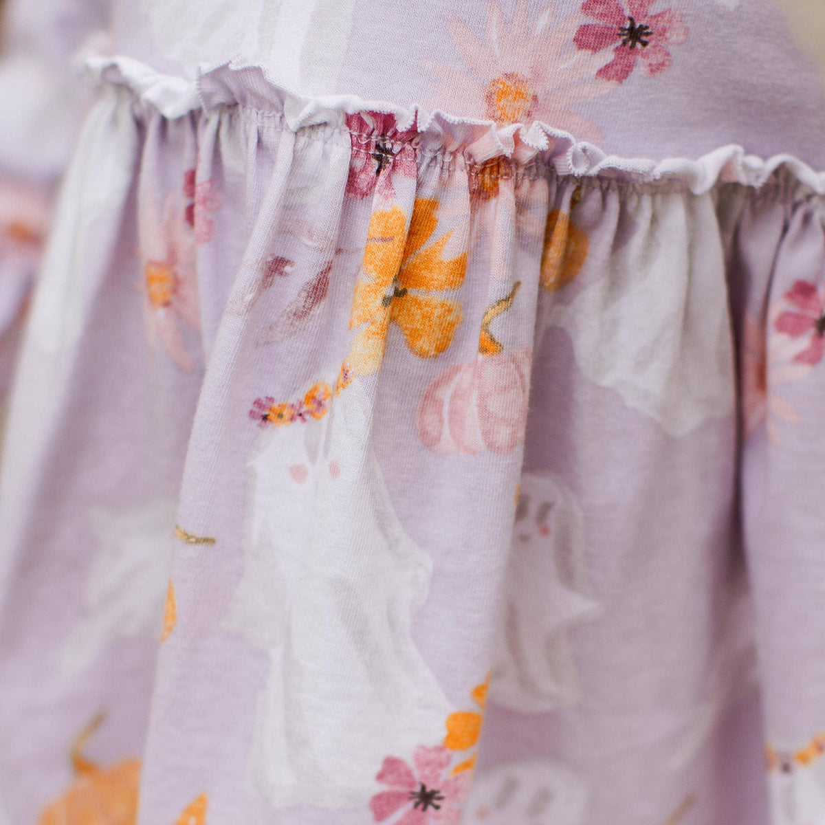 Close-up of a light lavender fabric with a ghost and floral print, featuring a ruffled elastic waistband.