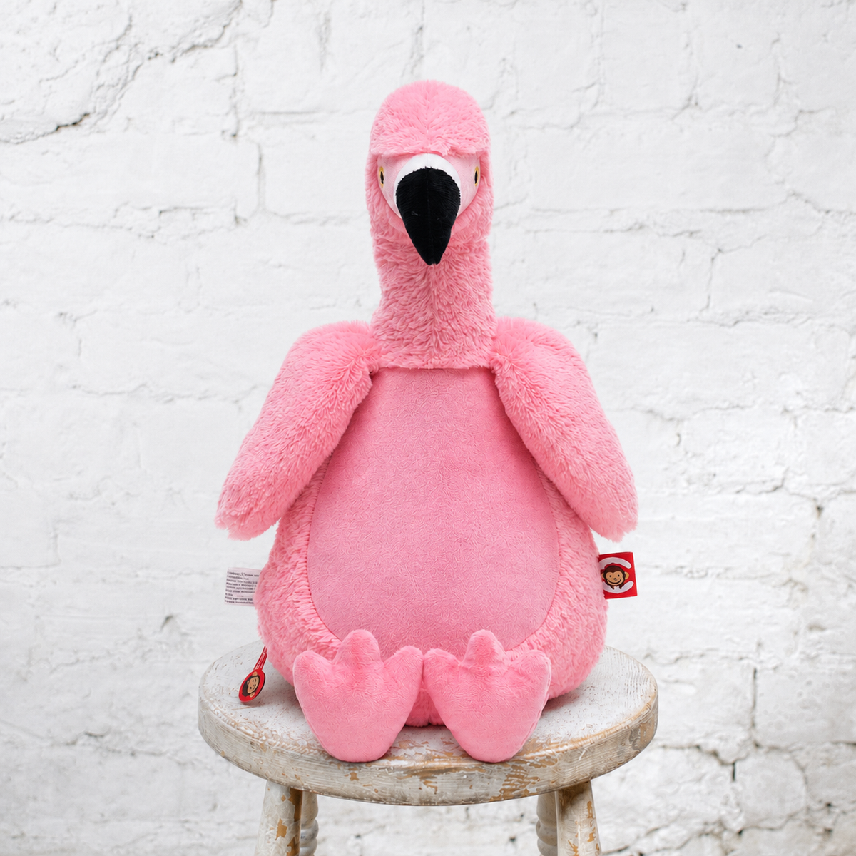 pink stuffed flamingo sits on a stool with a white wall in the background