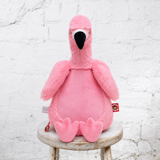 pink stuffed flamingo sits on a stool with a white wall in the background
