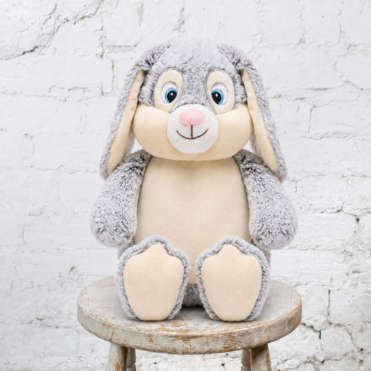 Grey bunny with cream stomache and ears on a stool with a white wall behind